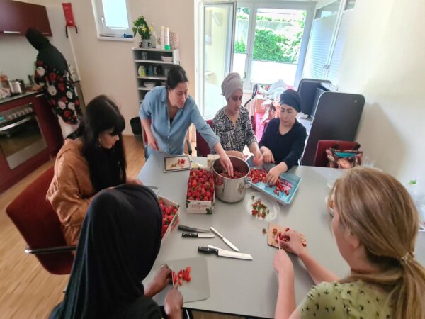 Unterschiedliche Frauen sitzen an einem Tisch und schneiden Erdbeeren